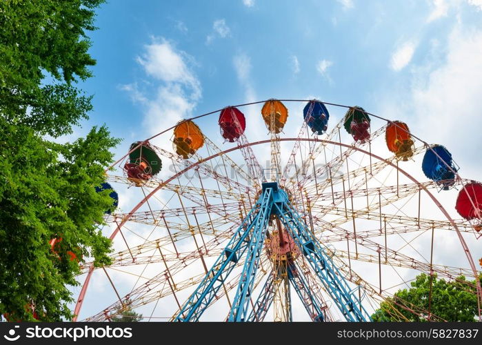 Ferris wheel in the green park over blue sky with clouds