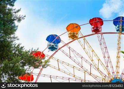 Ferris wheel in the green park over blue sky with clouds