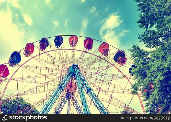Ferris wheel in the green park over blue sky with clouds. Instagram filter