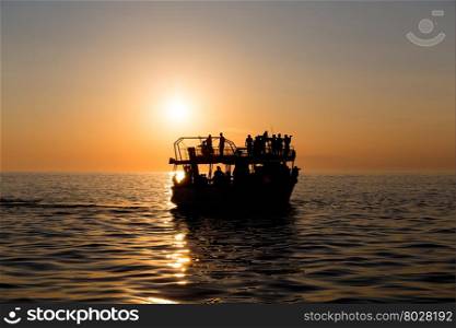 Ferry boat silhouette with people passengers at sunset sun in mediterranean sea