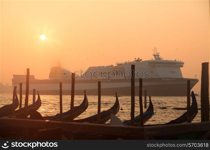 Ferryboat sailing near venetian gondolas at sunrise