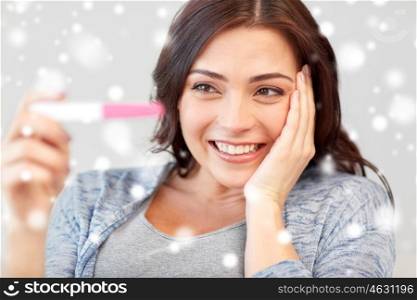 fertility, winter, maternity and people concept - happy smiling woman looking at pregnancy test at home over snow