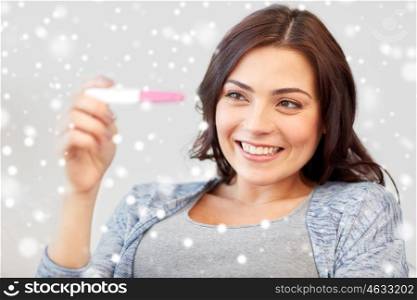 fertility, winter, maternity and people concept - happy smiling woman looking at pregnancy test at home over snow