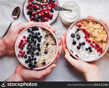 Festive and healthy breakfast for loved ones. Vintage bowls, cornflakes, granola, yogurt, fresh berries and hands of a young couple. Close-up, top view. Concept of healthy and delicious food. Festive and healthy breakfast for loved ones