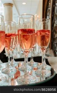 Festive champagne flutes filled with sparkling wine and floating strawberries with a backdrop bokeh of romantic twinkling party lights. Festive champagne flutes filled with sparkling wine and floating strawberries romantic twinkling party lights