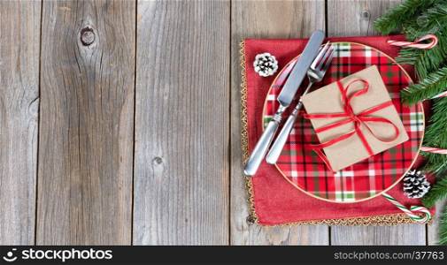 Festive Christmas dinner setting with evergreen branches and gift on top of rustic wood. Top view with copy space.