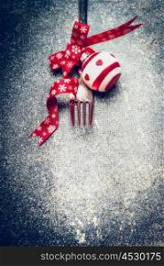 Festive Christmas table place setting with fork, red ribbon and ball on dark rustic vintage background, top view, close up