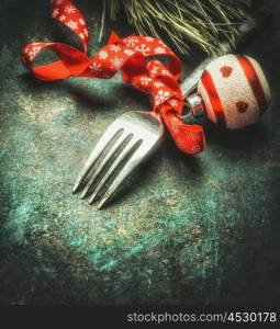 Festive Christmas table place setting with fork, ribbon ,ball and pine on dark rustic vintage background, top view, close up