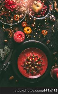 Festive Christmas table with red plates decorated with snowflakes, fir branches, burning candles , dried fruits, apples and spices, top view. Candle lighting bokeh. Cozy home Christmas dinner