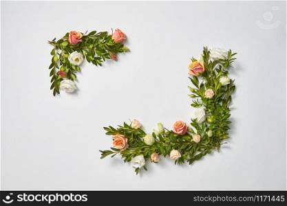 Festive corner frame with evergreen branches of boxwood with coral roses flowers on a light grey background, place for text. Flat lay. Valentine&rsquo;s Day greeting card.. Horizontal corner frame from evergreen twigs and flowers.
