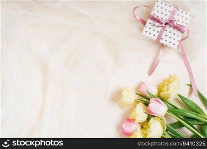 Festive floral arrangement of spring tulips and gift box on a beige fabric background. Top view from above, flat position. Space for copying. The concept of Birthday, Mother&rsquo;s Day, Valentine&rsquo;s Day, Women&rsquo;s Day, Wedding Day.
