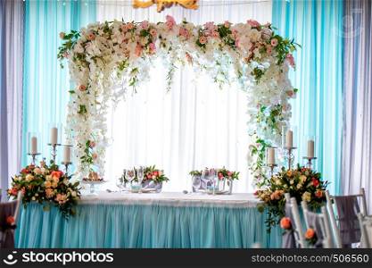 Festive room decorated with flowers. Wedding table setting with bouquets of flowers, candles, glasses and dishes. Decorations and setting for wedding party in restaurant.