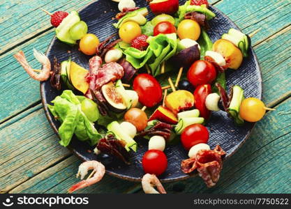Festive snack of shrimps, jamon, fruits and vegetables on wooden skewers.. Wooden skewers with shrimps, meat and fruits