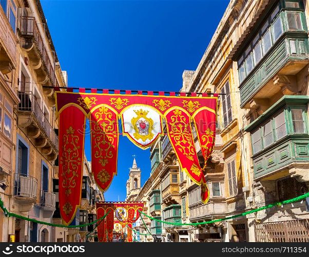 Festive standards and flags in the medieval narrow streets of Valletta on a sunny morning. Malta.. Malta. Holiday standards and flags in the old narrow streets of Valletta.