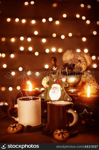 Festive still life on the table, beautiful glowing garland on the wall, two mugs with tea with homemade gingerbread, burning candle, Christmas decoration
