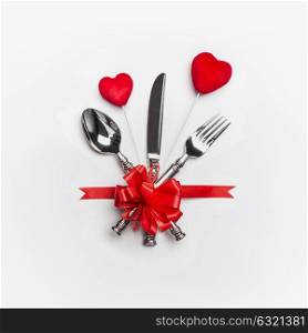 Festive table place setting with cutlery and red bow and two hearts on white background. Layout for Valentines day dinner invitation or anniversary, banquet, celebration, event