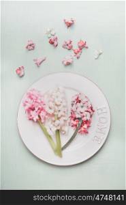 Festive table place setting with hyacinths and plate on light pastel wooden background, top view.
