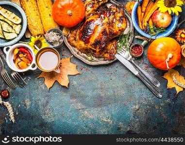 Festive Thanksgiving Day food background with roasted whole turkey or chicken and sauce, harvest vegetables: corn, pumpkin,carrots with cutlery on dark rustic kitchen table, top view, border