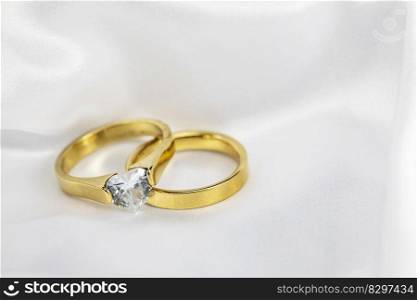 Festive wedding background with two gold rings with diamond on white satin material. Copy space. space for text. Festive wedding background with two gold rings with diamond on white satin material. Copy space.