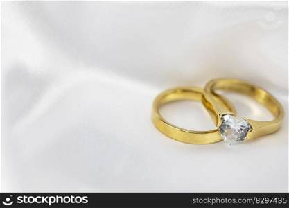 Festive wedding background with two gold rings with diamond on white satin material. Copy space. space for text. Festive wedding background with two gold rings with diamond on white satin material. Copy space.