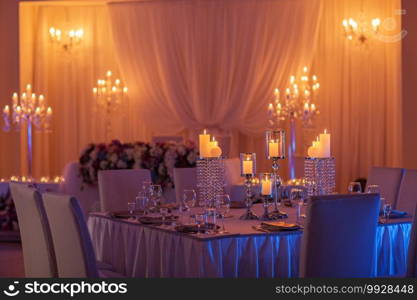 festive wedding table with burning candles, crystal, plates and glasses in yellow light. Crystal candle holder as a center piece at a wedding reception. festive wedding table with burning candles, crystal, plates and glasses in yellow light. Crystal candle holder as a center piece at a wedding reception.