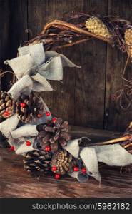 Festive wreath decoration. Woven from twigs and decorated with pine cones Christmas wreath on wooden background.