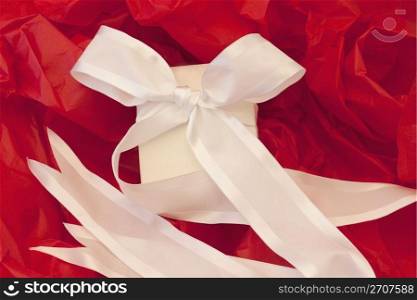 Festively elegant, wrapped white box and white ribbon against red tissue paper