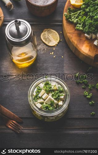 Feta cheese cubes jar with olives oil and herbs on dark rustic background. Marinated feta cheese. Homemade food. Country style. Top view