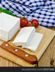 Feta cheese, knife, parsley, tomatoes, blue cloth on a wooden board