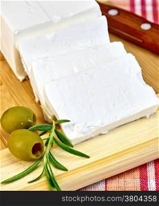 Feta cheese, knife, rosemary and olives on a wooden board on a background of red plaid fabric