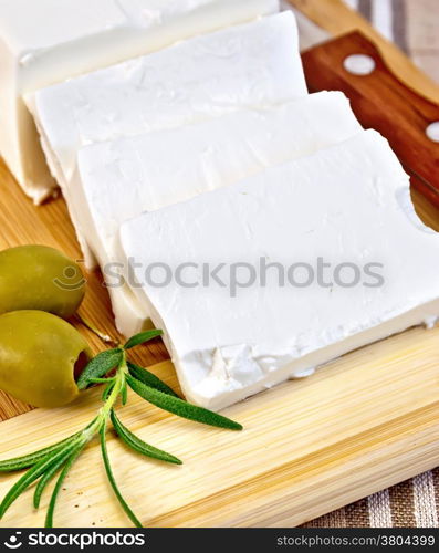 Feta cheese, knife, rosemary and olives on a wooden board on a background of brown checkered fabric