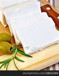 Feta cheese, knife, rosemary and olives on a wooden board on a background of brown checkered fabric