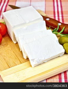 Feta cheese, knife, rosemary, olives and tomatoes on wooden board on a background of red plaid fabric