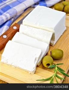 Feta cheese, knife, rosemary, olives, blue checkered napkin on the background of wooden boards