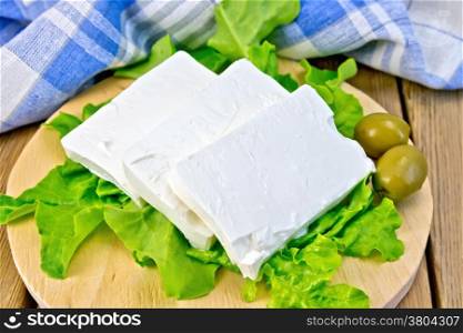 Feta cheese, lettuce, olives, blue checkered napkin on the background of wooden boards