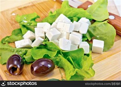 Feta cheese on green lettuce, olives, knife on background wooden board and cloth