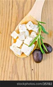 Feta cheese with spices in spoon, olives and rosemary on background wooden board