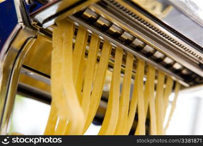 Fettuccine coming out of a manual pastamachine - shallow depth of field with focus on the pasta