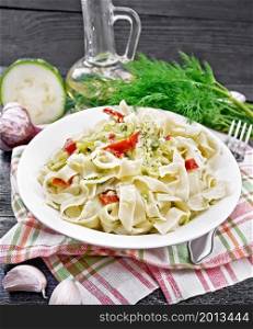 Fettuccine pasta with zucchini and hot red pepper in creamy sauce in white plate on a kitchen towel, garlic and fork on a wooden board background
