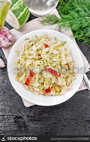 Fettuccine pasta with zucchini and hot red pepper in creamy sauce in white plate on a napkin, garlic and a fork on wooden board background from above