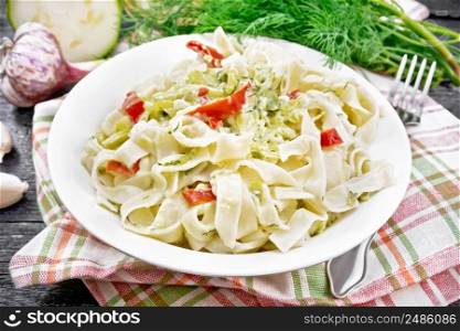 Fettuccine pasta with zucchini and hot red pepper in creamy sauce in white plate on a towel, garlic and a fork on black wooden board background