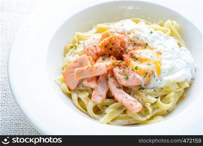 Fettucine with salmon, egg and parmesan cheese, served on white plate.