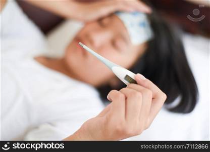 fever child with thermometer measuring temperature of kid sick / child with high fever and laying in bed hand holding on forehead and cooling gel sheet
