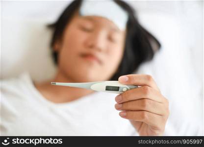 fever child with thermometer measuring temperature of kid sick / child with high fever and laying in bed hand holding on forehead and cooling gel sheet