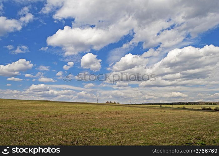 Field against beautiful sky with cumulus clouds, spring time