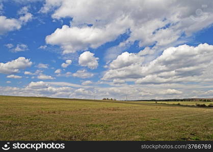 Field against beautiful sky with cumulus clouds, spring time