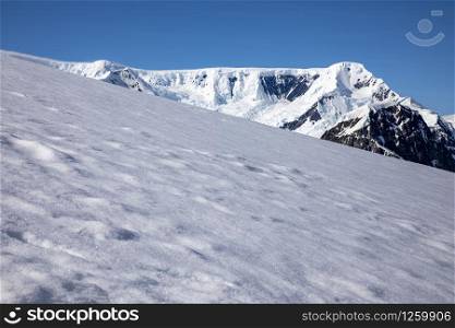 Field covered with snow and ice provides space for text space in front of mountains covered with glaciers