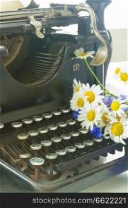 field fresh flowers and black vintage typewriter close up. typewriter on table
