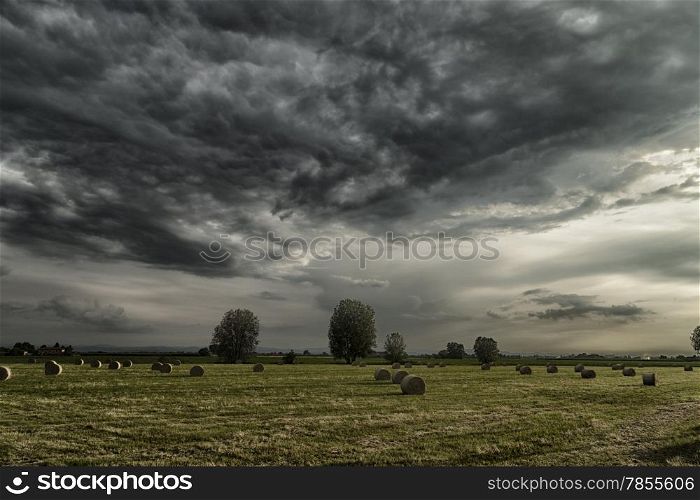 Field of hay bales in Romagna in Italy under dark clouds