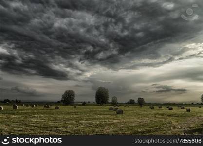 Field of hay bales in Romagna in Italy under dark clouds